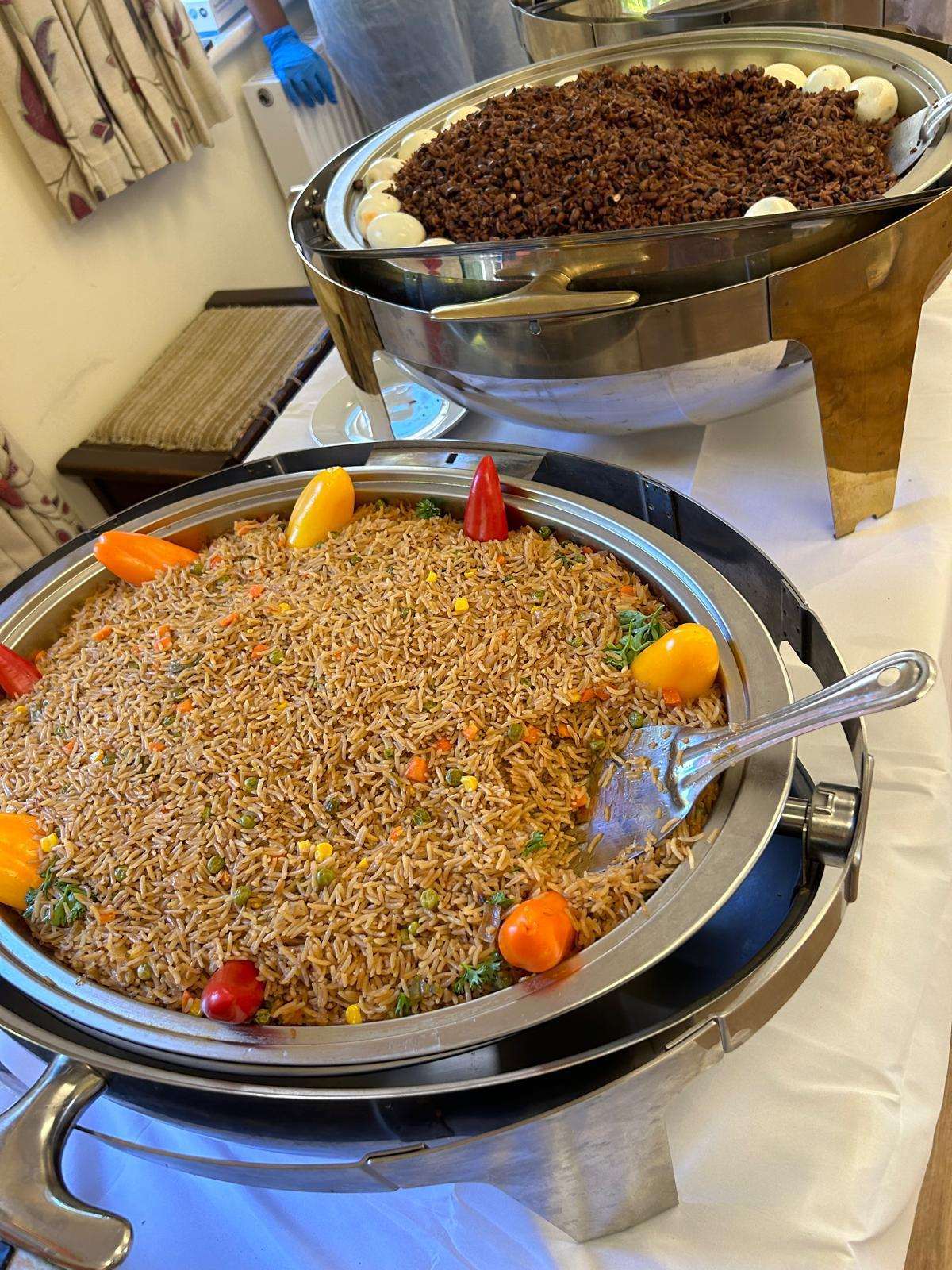 Ghanaian jollof rice and vegetable rice in chafing dishes, garnished with sweet peppers, at a Cynthia's African Dishes event buffet