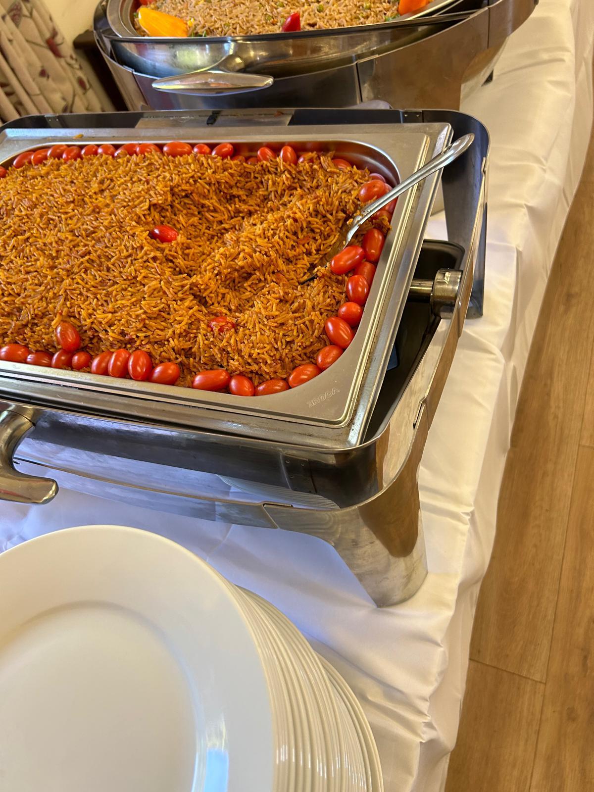 Tray of Ghanaian jollof rice edged with cherry tomatoes on a catering buffet line