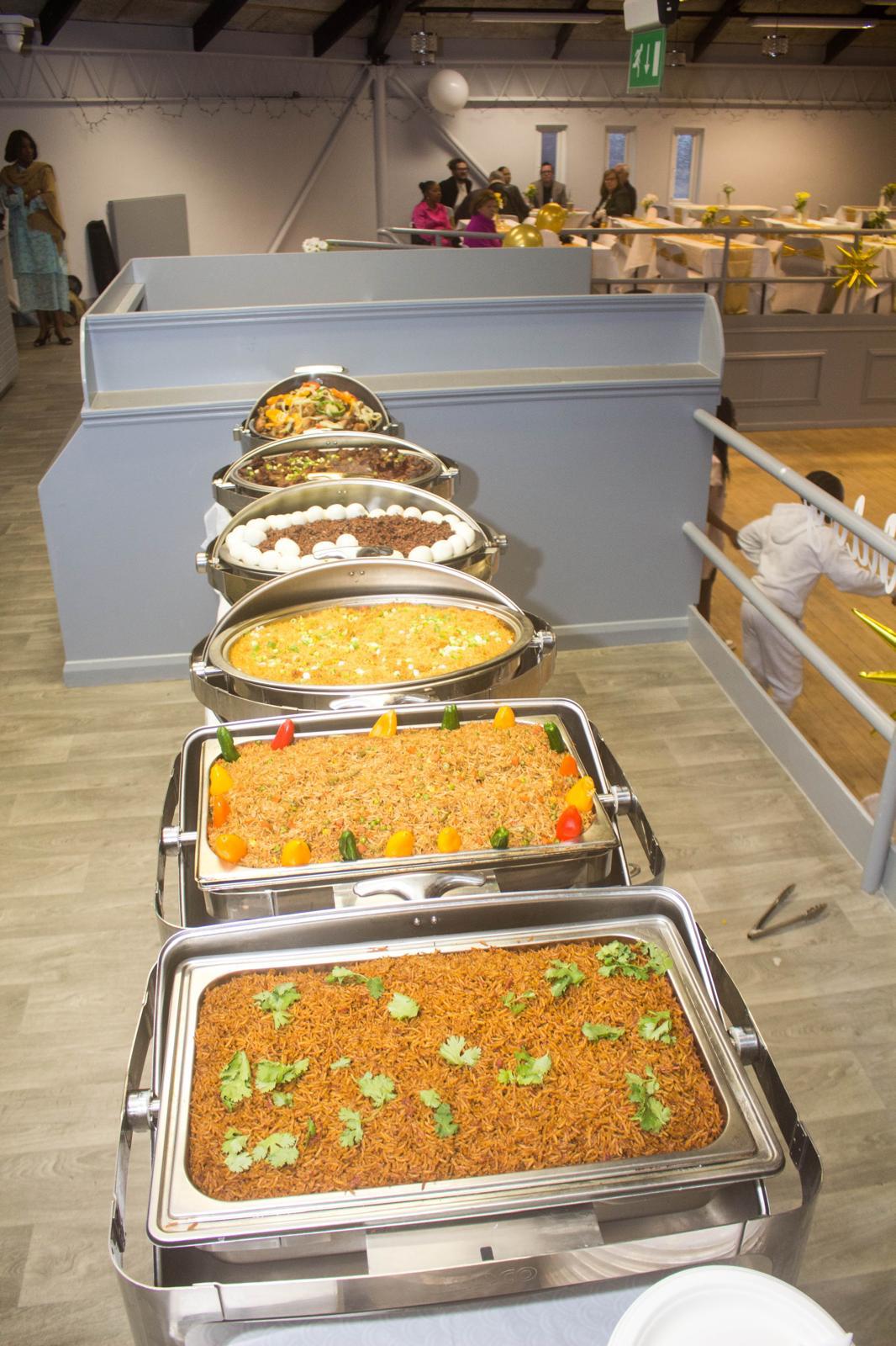 Full West African buffet line in an event hall, with jollof rice, waakye, fried rice and stews in chafing dishes