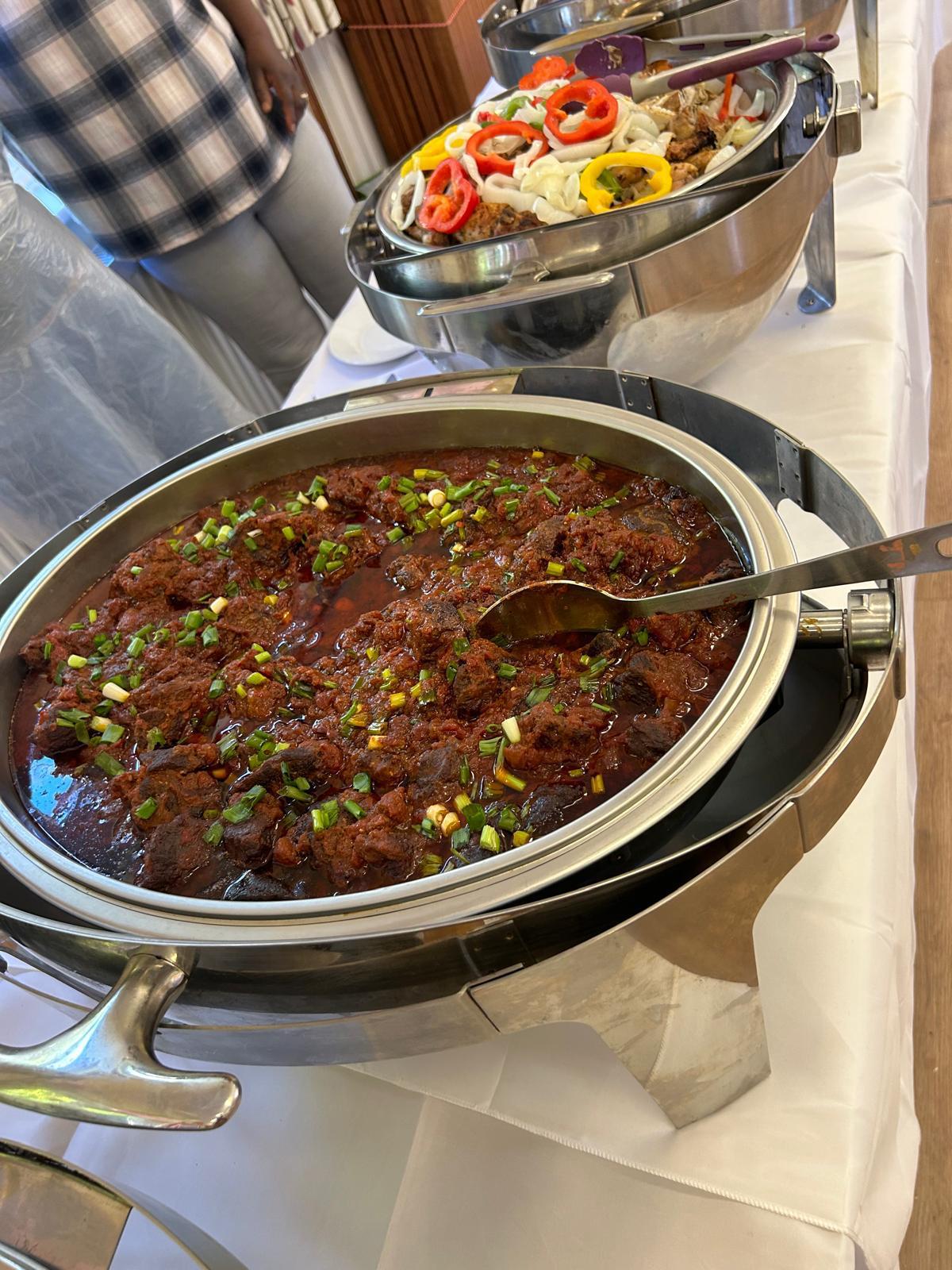 Close-up of slow-cooked Ghanaian beef stew garnished with spring onions in a chafing dish